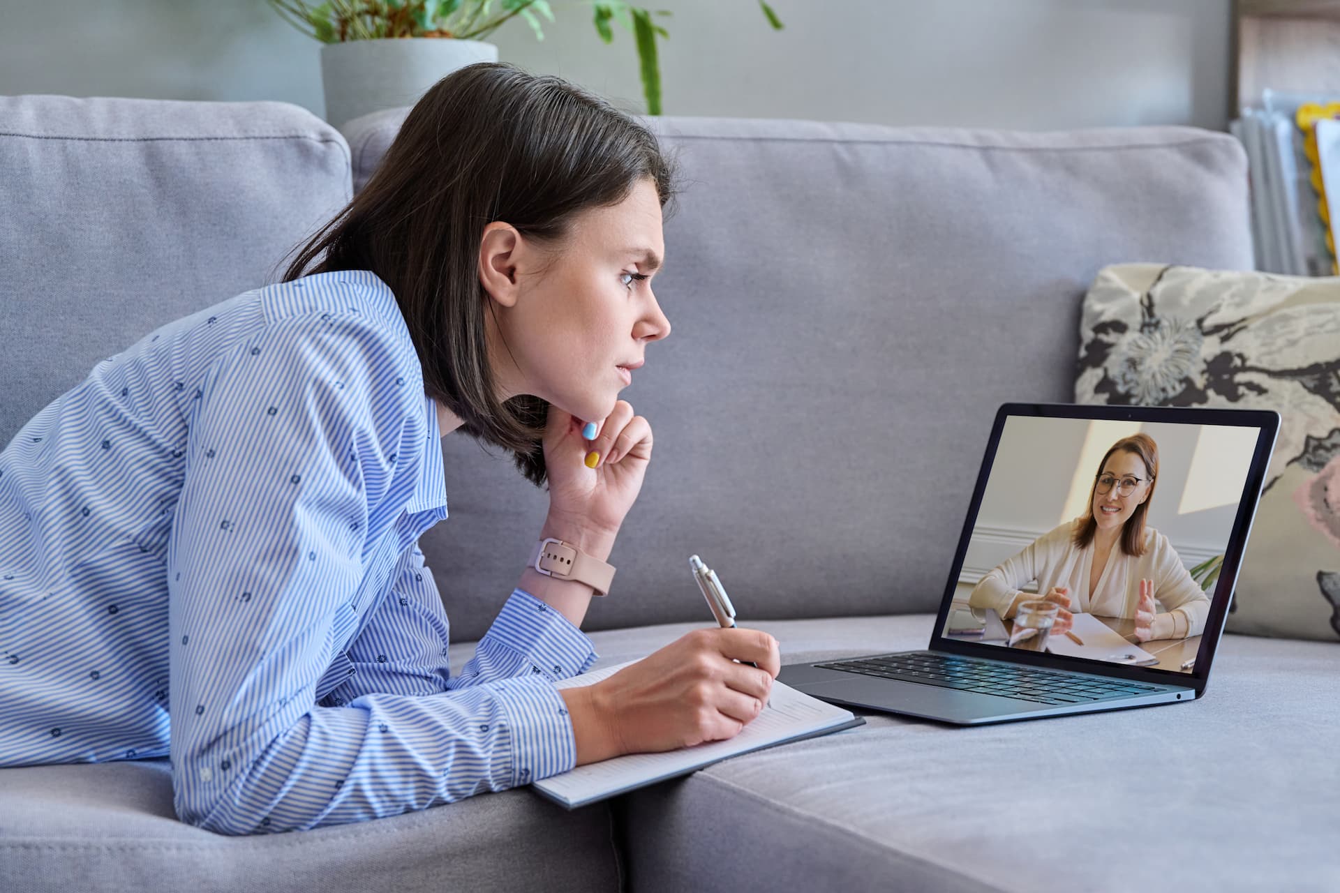 woman taking down notes while looking in to the laptop